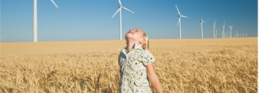 Girl stood in field in front of wind farm
